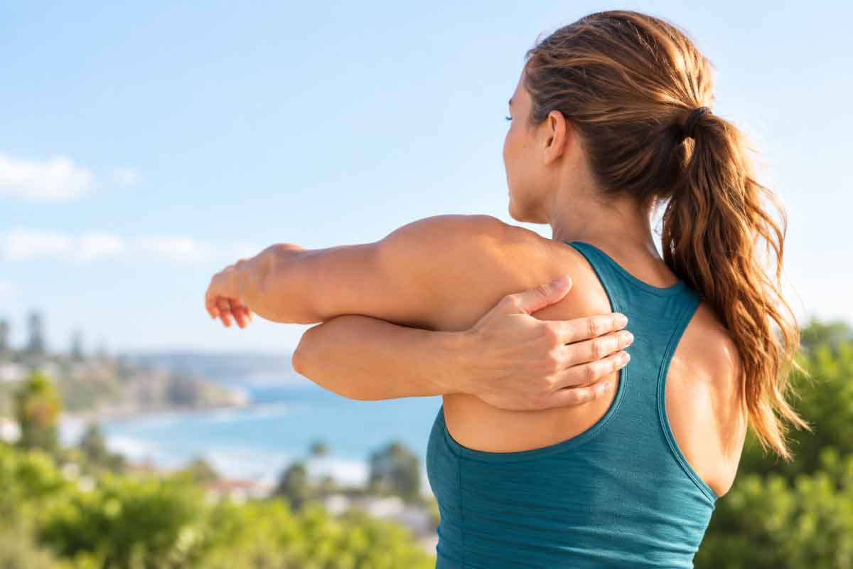 Woman performing a gentle cross-body shoulder stretch outdoors.
