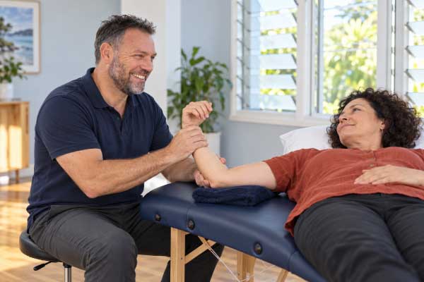 Scott Baines providing supported wrist manual therapy during a home physiotherapy appointment.